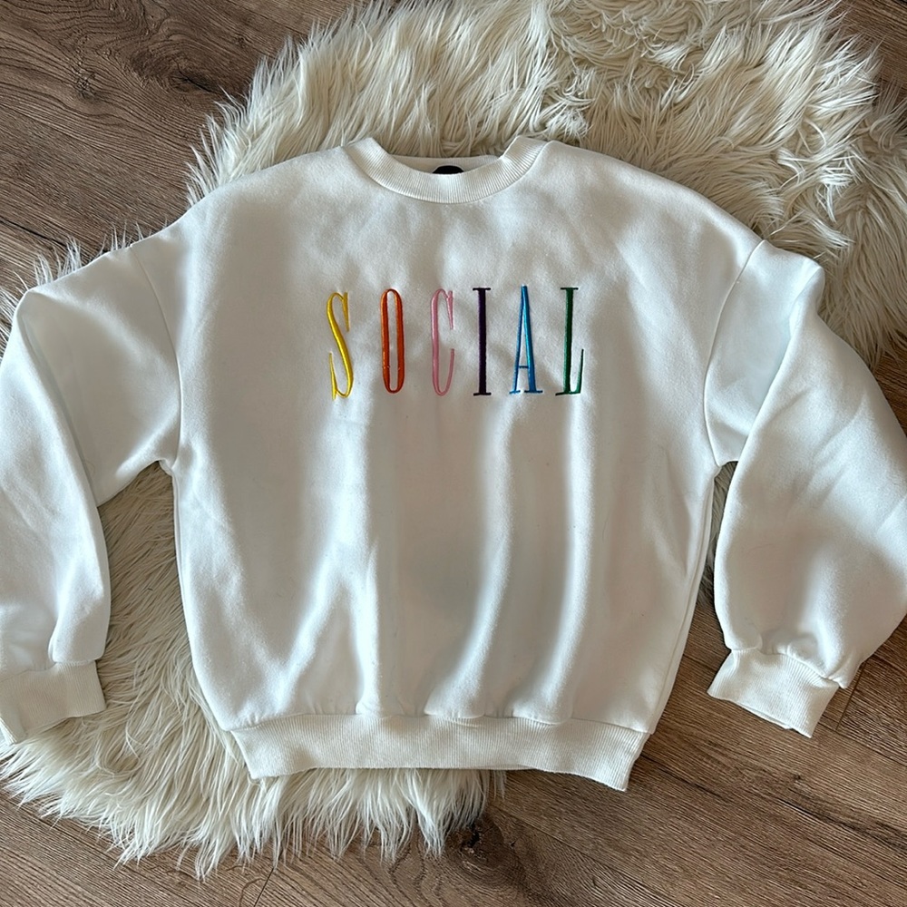 White sweatshirt. SOCIAL written in different colors on front.